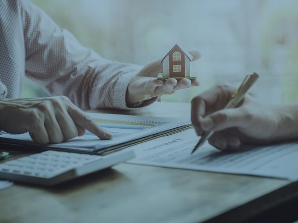 Pessoa segurando uma miniatura de casa e outra pessoa com caneta mão