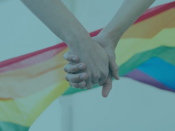 mãos dadas com bandeira lgbt ao fundo